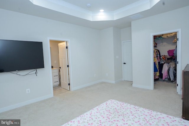 bedroom featuring a tray ceiling, a closet, light colored carpet, a spacious closet, and baseboards