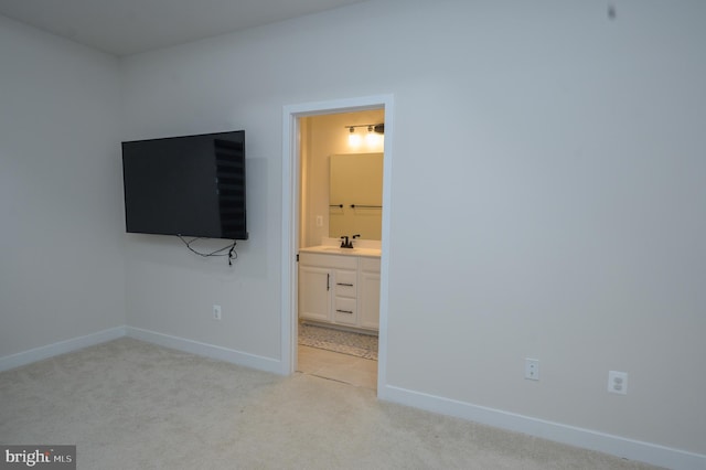 unfurnished bedroom featuring light carpet, a sink, ensuite bath, and baseboards