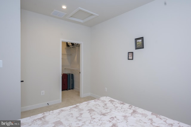 unfurnished bedroom with a walk in closet, light colored carpet, visible vents, attic access, and baseboards