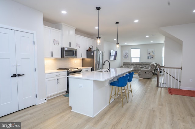 kitchen with stainless steel appliances, light countertops, open floor plan, a kitchen island with sink, and white cabinetry