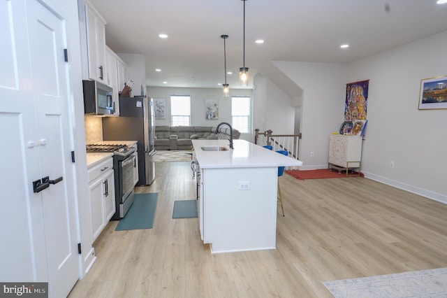 kitchen featuring stainless steel appliances, white cabinetry, open floor plan, light countertops, and an island with sink