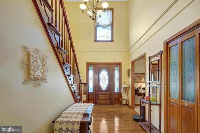 foyer with a high ceiling, stairway, wood finished floors, and a notable chandelier