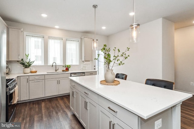 kitchen featuring appliances with stainless steel finishes, dark wood-type flooring, a center island, light countertops, and a sink