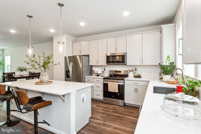 kitchen with stainless steel appliances, dark wood-style flooring, a sink, light countertops, and a center island