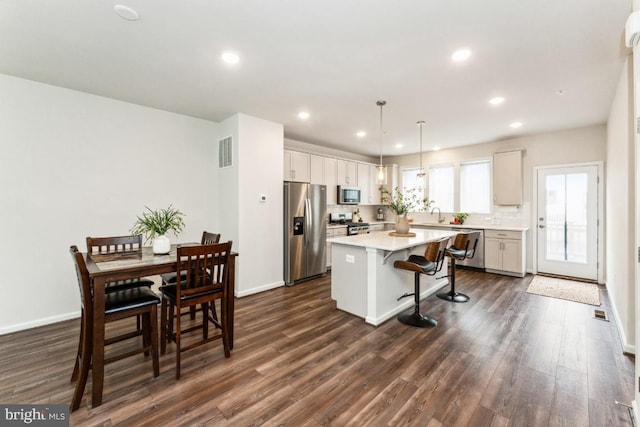 kitchen with visible vents, a kitchen island, dark wood-style flooring, stainless steel appliances, and a kitchen bar