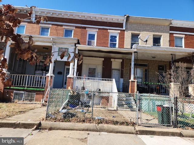 multi unit property featuring a fenced front yard, a gate, a porch, and brick siding