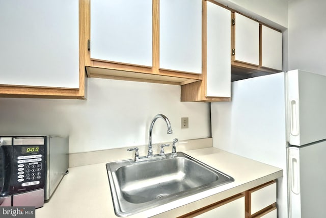 kitchen featuring a sink, white cabinetry, light countertops, freestanding refrigerator, and stainless steel microwave