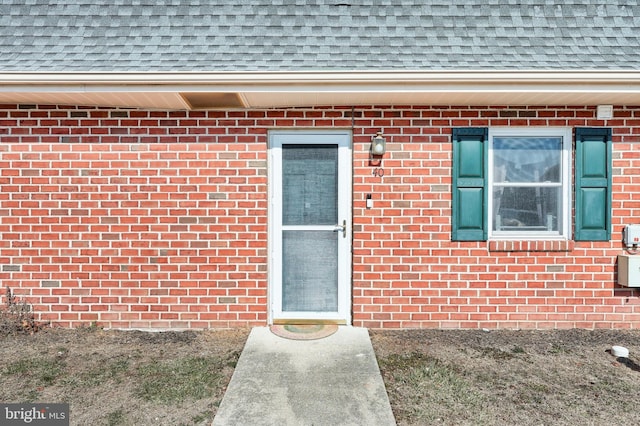 property entrance featuring roof with shingles and brick siding