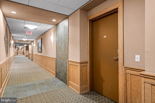 hallway with a paneled ceiling, carpet floors, and wainscoting