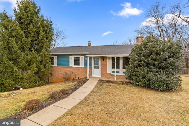 ranch-style home with a front lawn, a chimney, a shingled roof, and brick siding