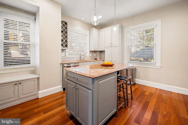 kitchen with stainless steel dishwasher, gray cabinets, a kitchen bar, and wood finished floors