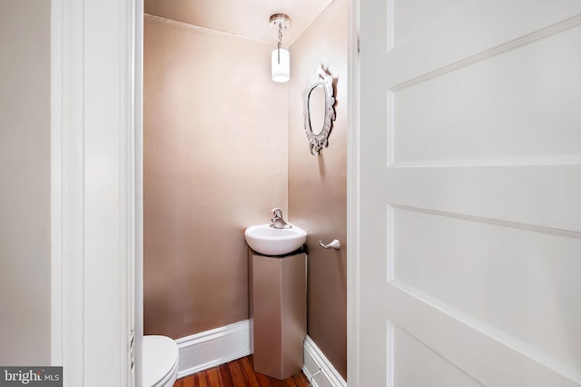 half bathroom featuring a sink, baseboards, toilet, and wood finished floors