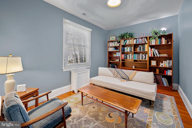 sitting room with radiator, wood finished floors, visible vents, and baseboards