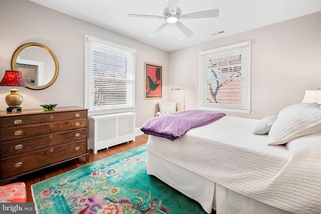 bedroom with dark wood-type flooring, radiator, visible vents, and ceiling fan