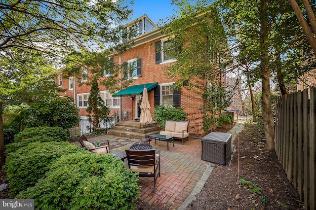 back of house with fence private yard, an outdoor living space with a fire pit, a patio, and brick siding