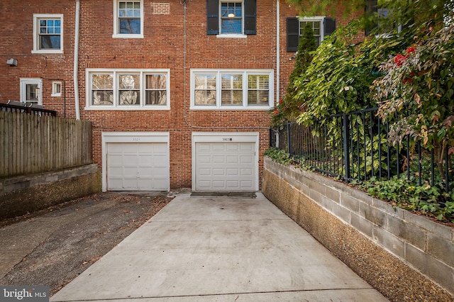 back of property with concrete driveway, brick siding, an attached garage, and fence