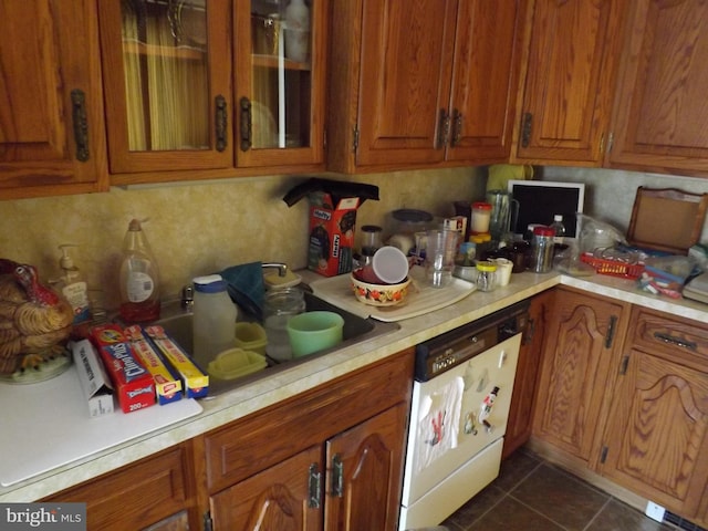 kitchen with glass insert cabinets, brown cabinets, white dishwasher, light countertops, and dark tile patterned floors