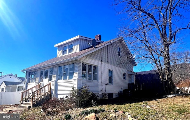 view of front of home with a chimney, roof with shingles, and fence