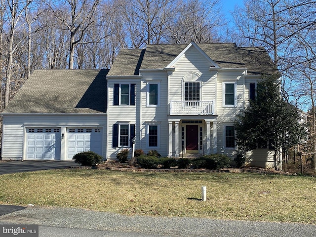 colonial house with driveway, a garage, a balcony, roof with shingles, and a front yard