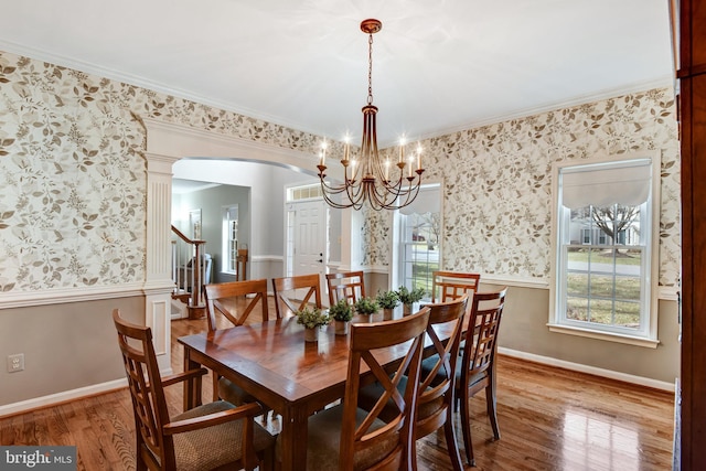 dining space with wallpapered walls, arched walkways, wood finished floors, and wainscoting