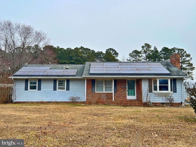 ranch-style home with solar panels, a front lawn, a chimney, and brick siding