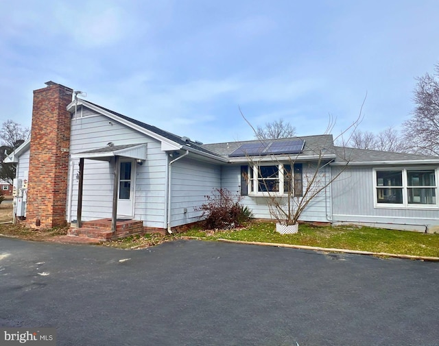 view of front of house featuring a shingled roof, roof mounted solar panels, and a chimney