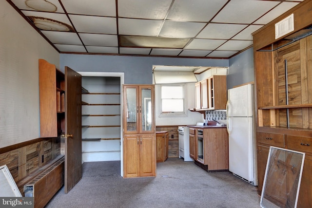 kitchen featuring visible vents, radiator heating unit, light carpet, white appliances, and a drop ceiling