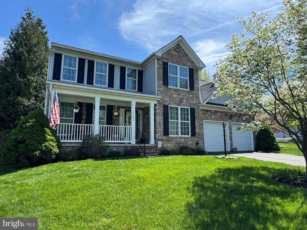 traditional home with a front lawn, an attached garage, driveway, stone siding, and a porch