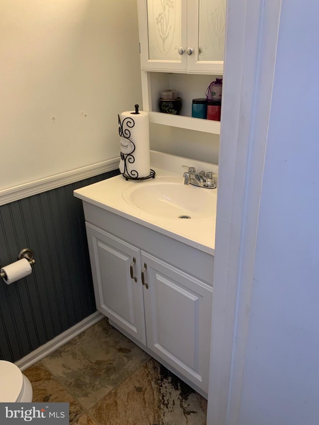 half bathroom featuring vanity, wainscoting, and toilet