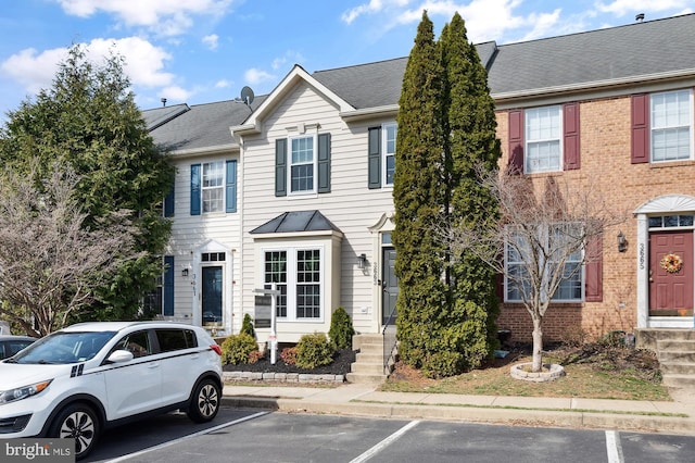 townhome / multi-family property featuring brick siding, roof with shingles, and uncovered parking