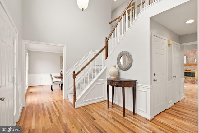 entryway with light wood-type flooring, a wainscoted wall, stairs, and a high ceiling