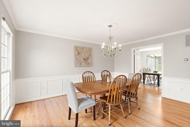 dining area with ornamental molding, light wood finished floors, wainscoting, and an inviting chandelier