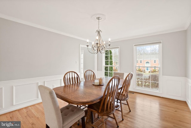 dining area with light wood finished floors, ornamental molding, a chandelier, and wainscoting