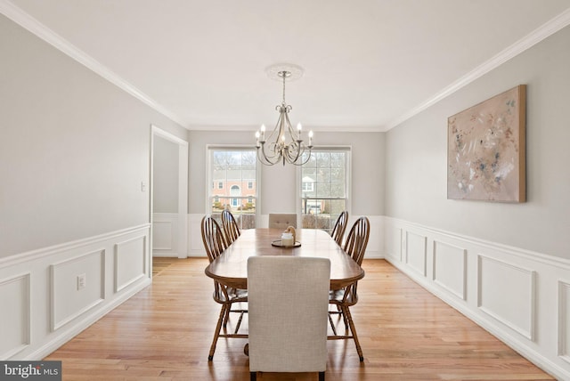 dining room featuring light wood-style floors, crown molding, a decorative wall, and a notable chandelier