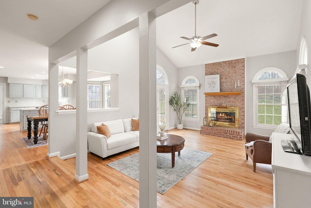 living area featuring baseboards, light wood-type flooring, a brick fireplace, and a healthy amount of sunlight