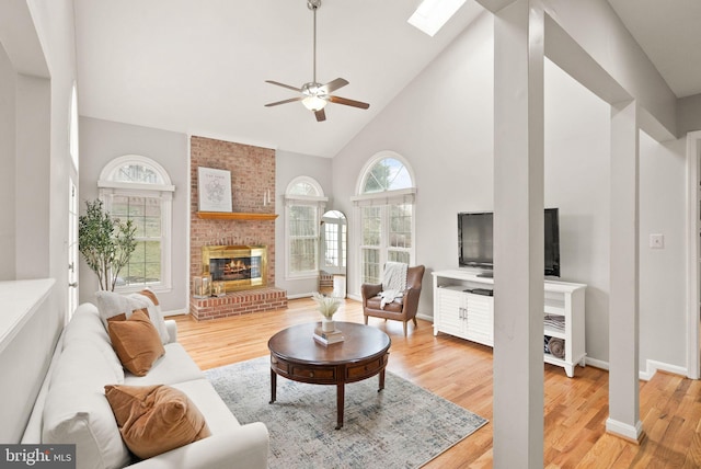 living room featuring a skylight, a fireplace, light wood finished floors, high vaulted ceiling, and baseboards