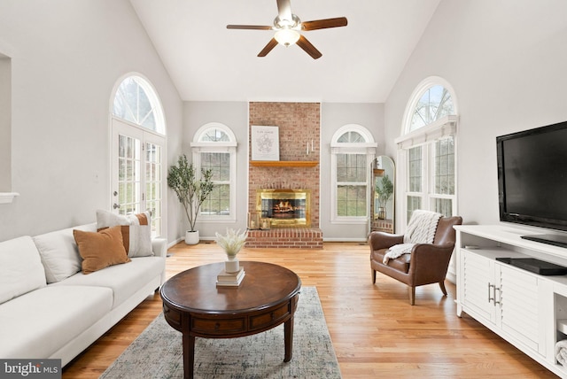 living room with light wood-type flooring, a fireplace, high vaulted ceiling, and a ceiling fan