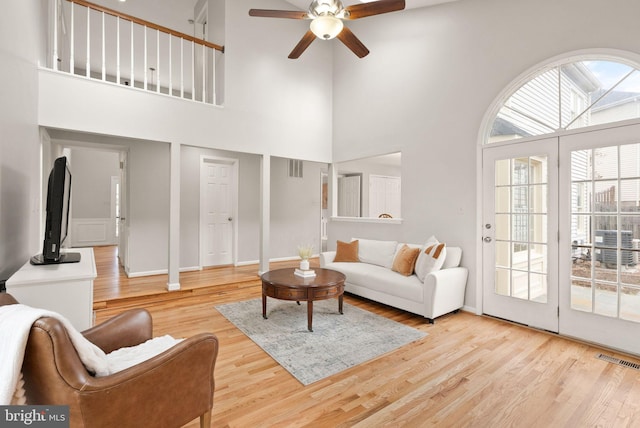 living room with a ceiling fan, visible vents, a high ceiling, and wood finished floors