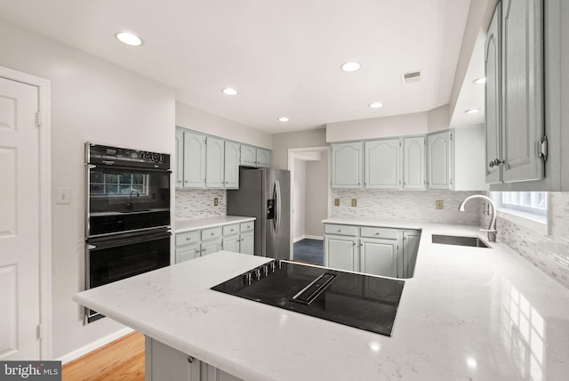 kitchen featuring visible vents, decorative backsplash, a sink, a peninsula, and black appliances