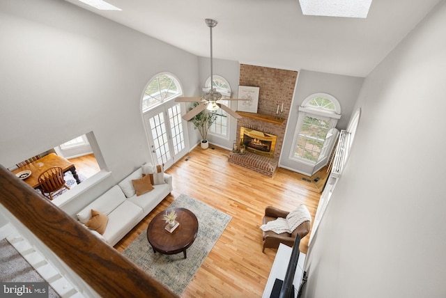 living area featuring vaulted ceiling with skylight, a fireplace, wood finished floors, and a ceiling fan