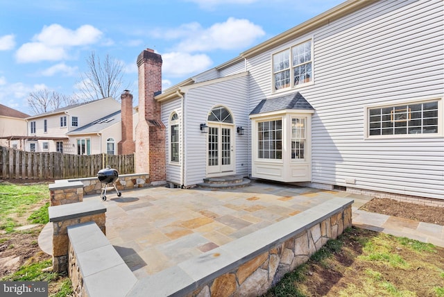 rear view of house featuring entry steps, a chimney, fence, and a patio