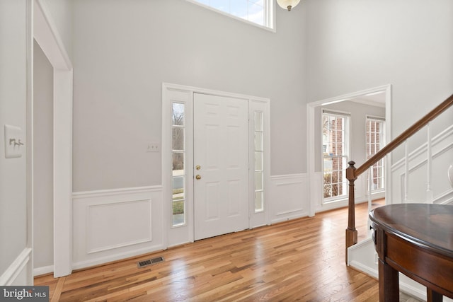 foyer with stairway, visible vents, wood finished floors, and wainscoting