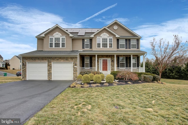 view of front facade featuring driveway, stone siding, an attached garage, covered porch, and roof mounted solar panels