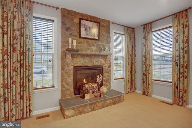 living area featuring carpet floors, visible vents, a stone fireplace, and baseboards