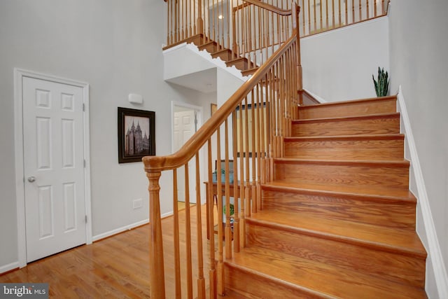 stairs with a high ceiling, baseboards, and wood finished floors