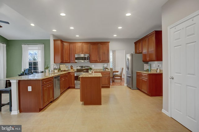 kitchen with a kitchen island, appliances with stainless steel finishes, light stone counters, a peninsula, and a sink