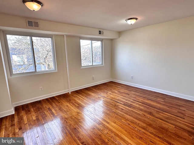 empty room featuring visible vents, baseboards, and wood-type flooring