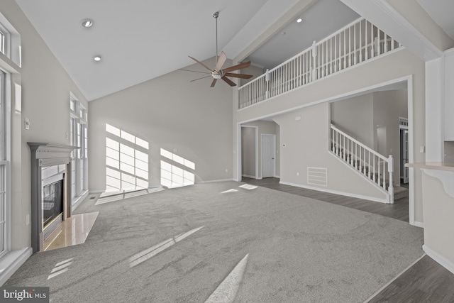 unfurnished living room with visible vents, dark carpet, stairway, a high end fireplace, and high vaulted ceiling