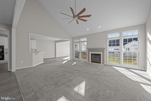 unfurnished living room with baseboards, a ceiling fan, a fireplace with flush hearth, carpet floors, and high vaulted ceiling