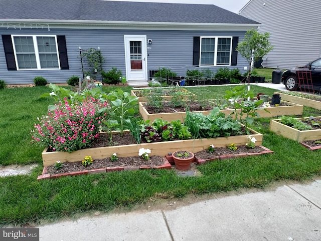 ranch-style home featuring a garden, roof with shingles, and a front lawn